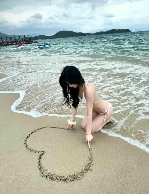 Cô gái bikini ngồi trên cát trắng.